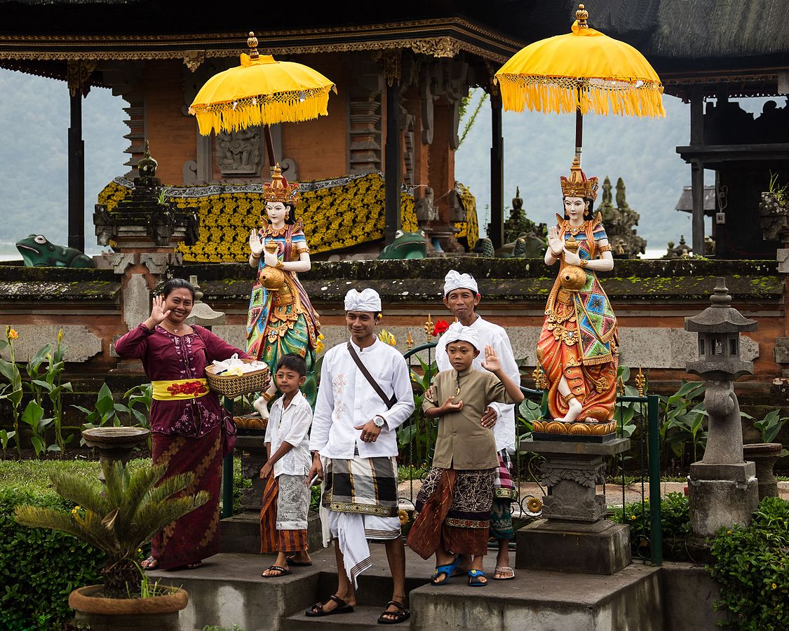  A group of people in traditional Balinese dress pose for a photo in front of a temple with two statues.
